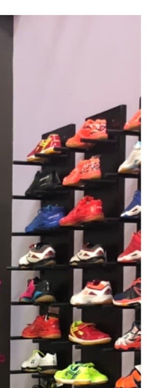 Rows of badminton shoes displayed on the pro shop's wall rack, with a bench underneath for trying them on.