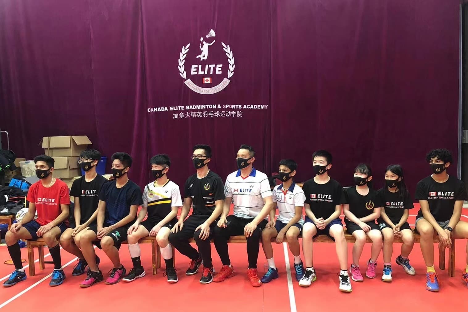 A group of coaches and students seated together on benches in front of the club's Academy backdrop wall.